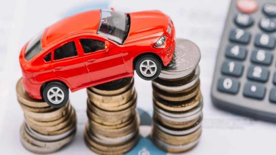 Imagen ilustrativa. Auto de juguete sobre tres pilas de monedas y una calculadora